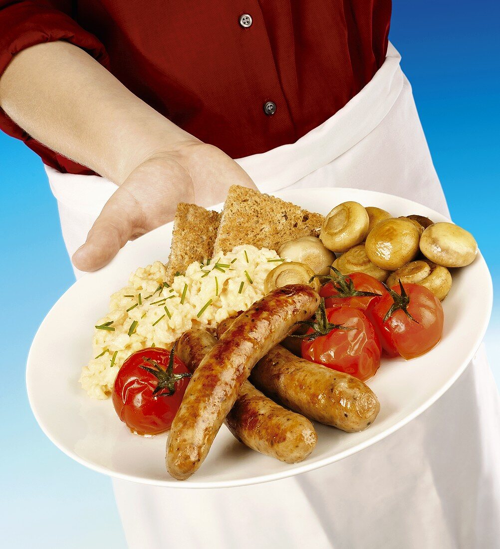 Waiter with plate of sausages, scrambled egg & vegetables