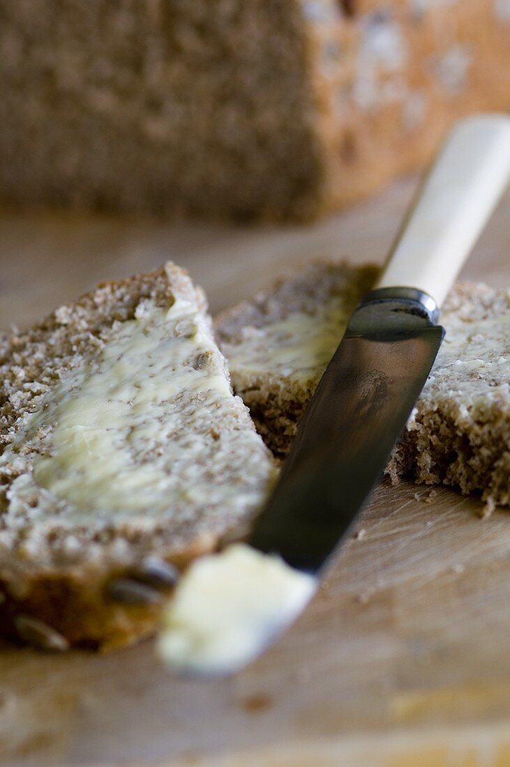 A halved slice of bread and butter with knife