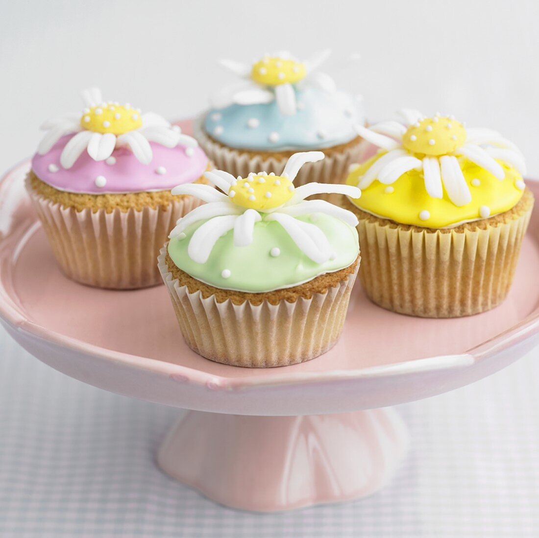 Four cupcakes with daisy decorations on a pedestal stand