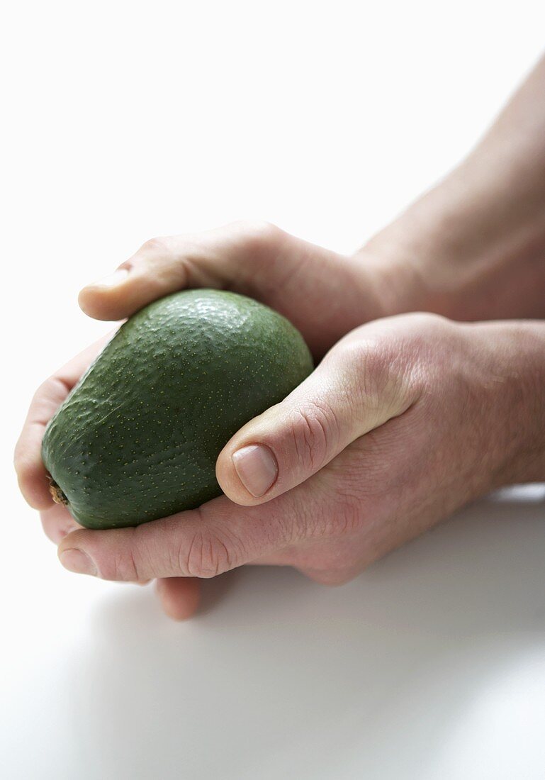 Two hands holding an avocado