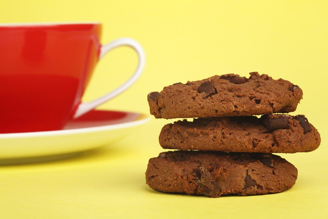 Three chocolate chip cookies with a cup and saucer