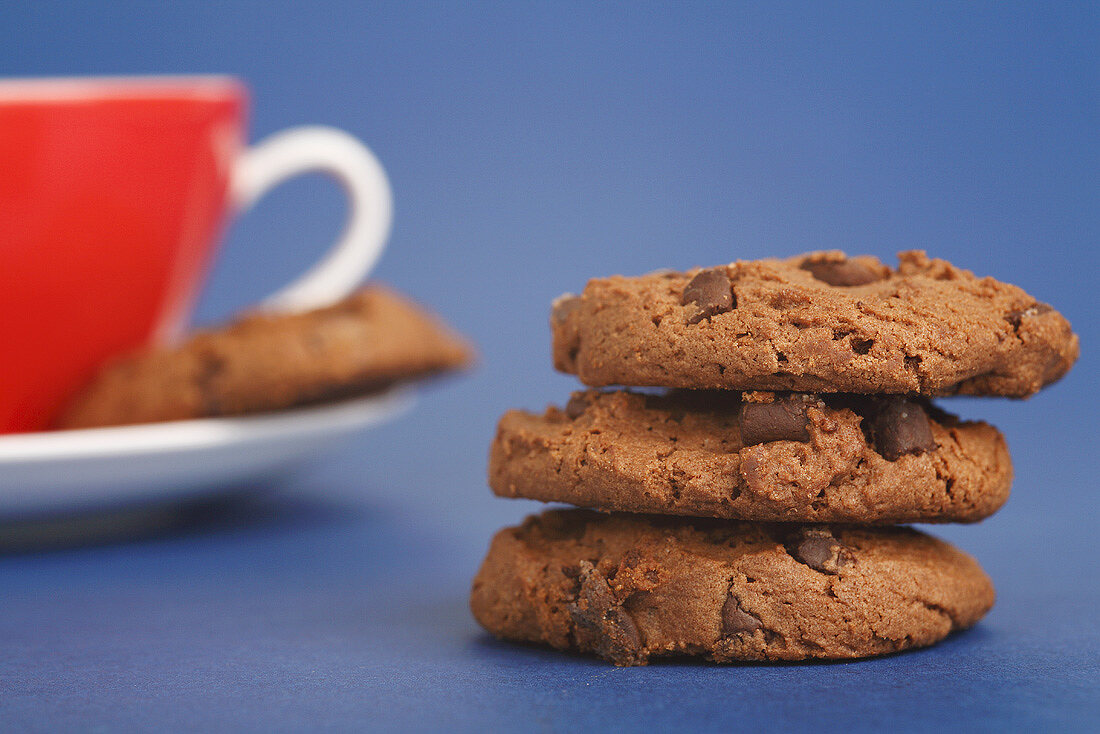 A pile of three chocolate chip cookies with a cup & saucer