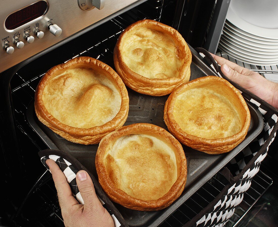 Mann holt gebackene Yorkshire Puddings aus dem Ofen