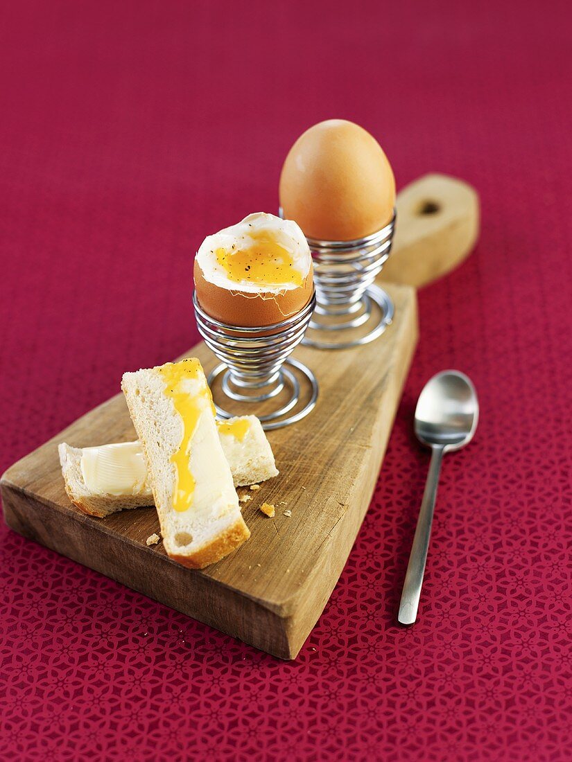 Frühstückseier im Eierbecher mit Toast-Streifen auf Holzbrett