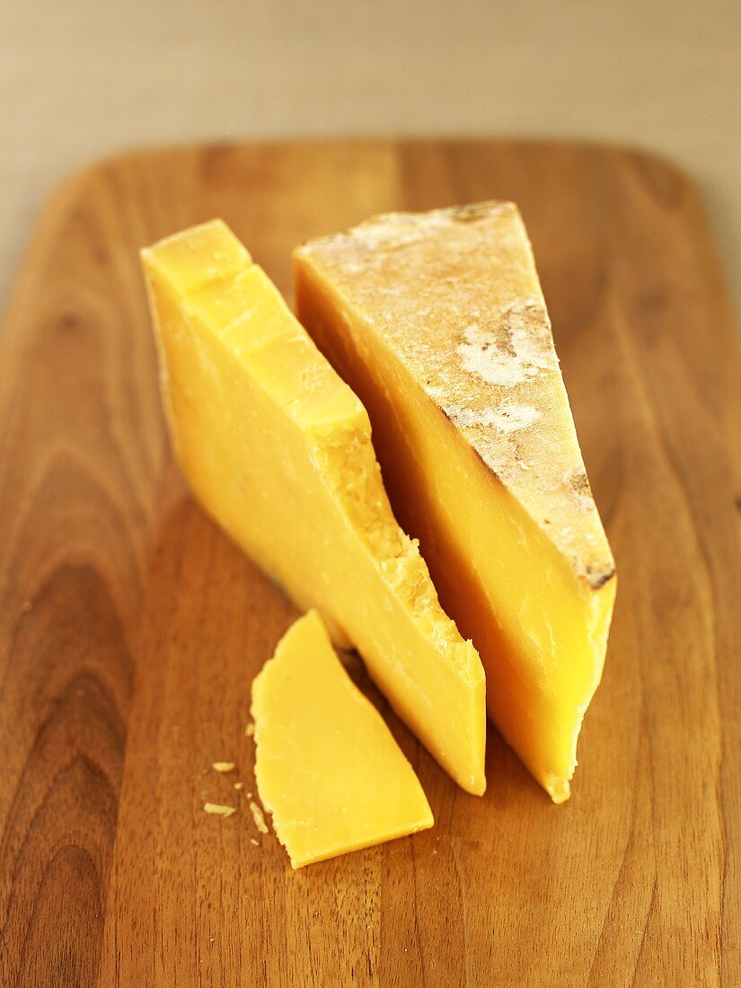 Pieces of Cheddar cheese on a wooden board