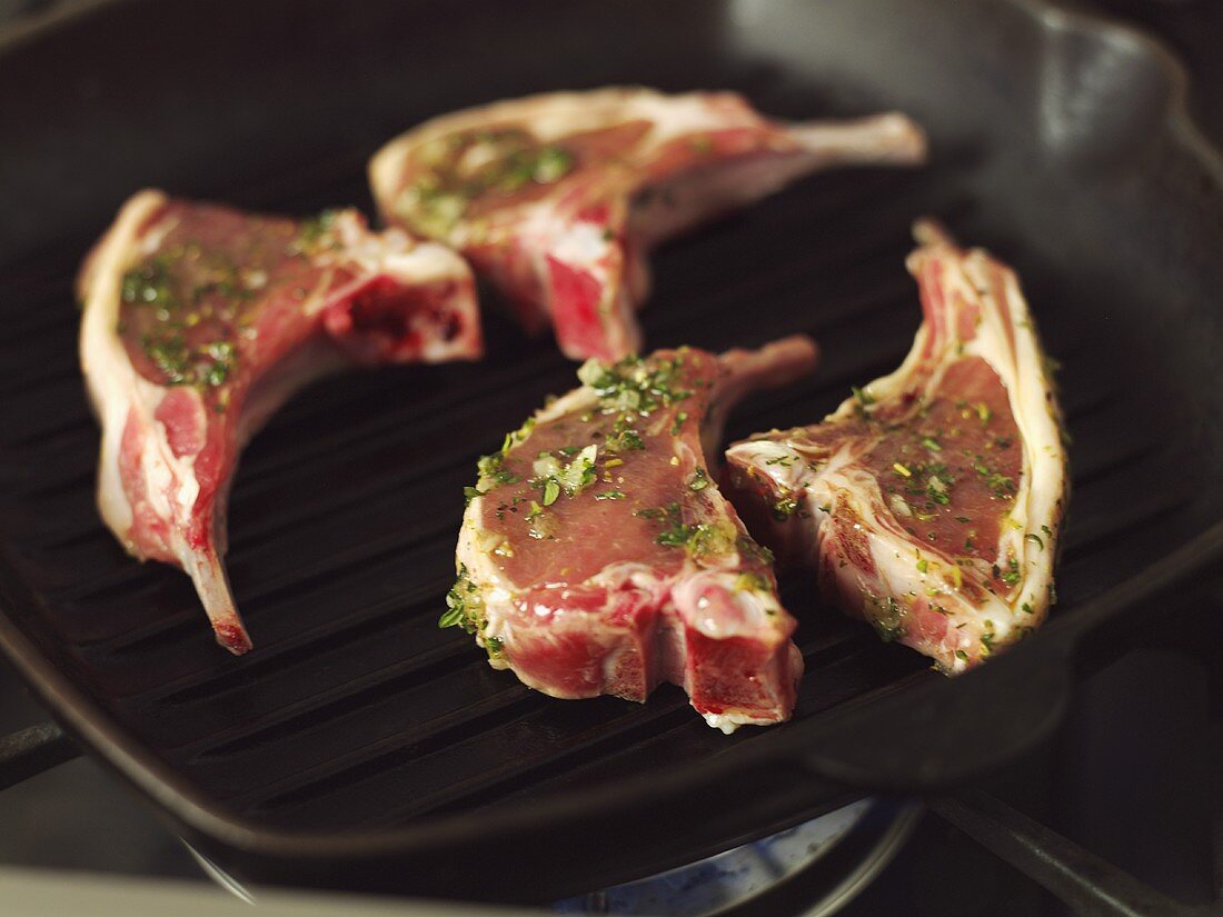 Four raw, marinated lamb chops in a grill pan