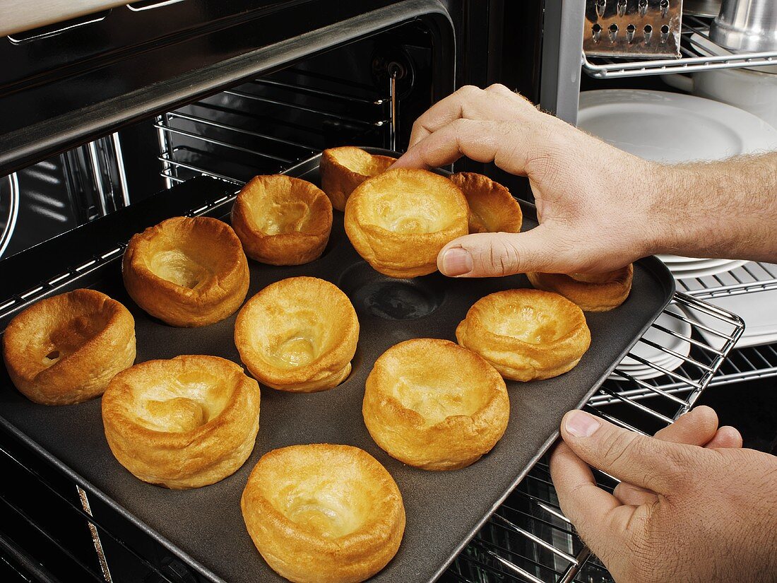 Mann holt gebackene Yorkshire Puddings aus dem Ofen