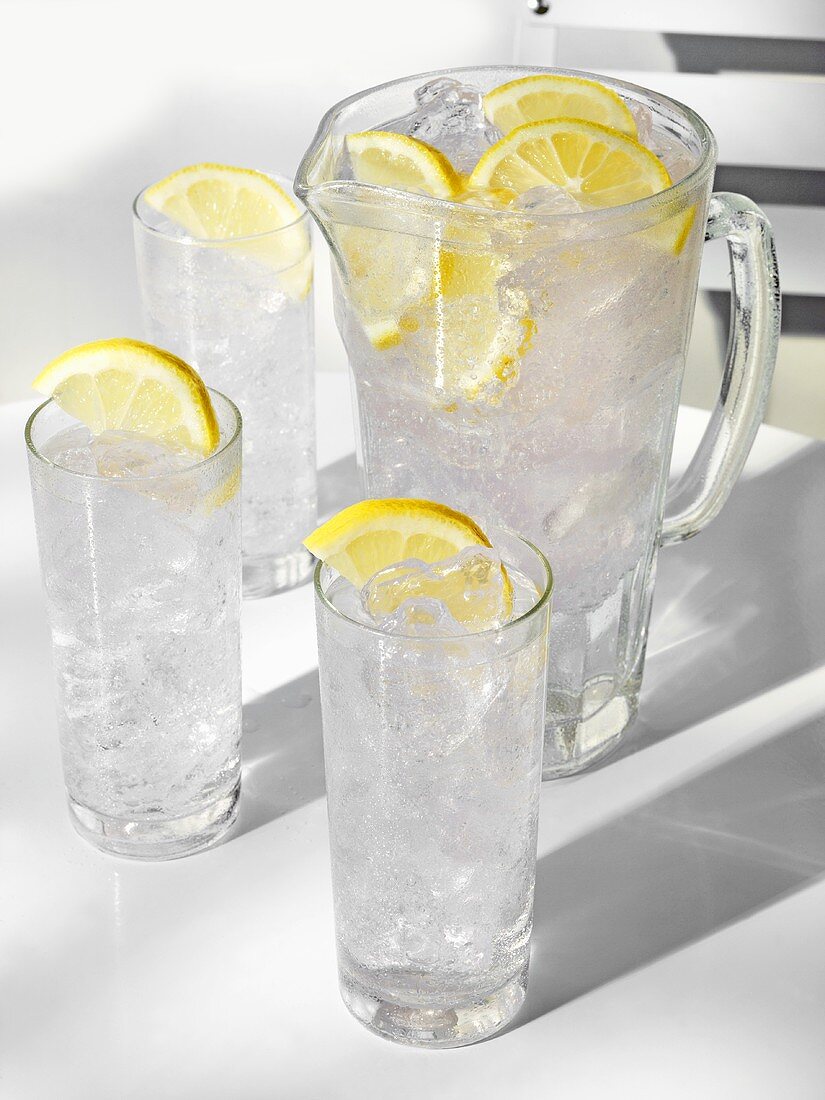 Water in glasses and jug, with ice cubes and lemon slices
