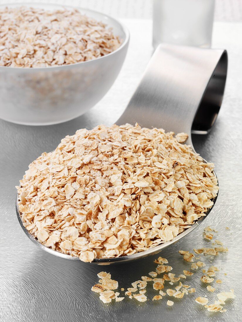 Rolled oats on a spoon and in a glass bowl