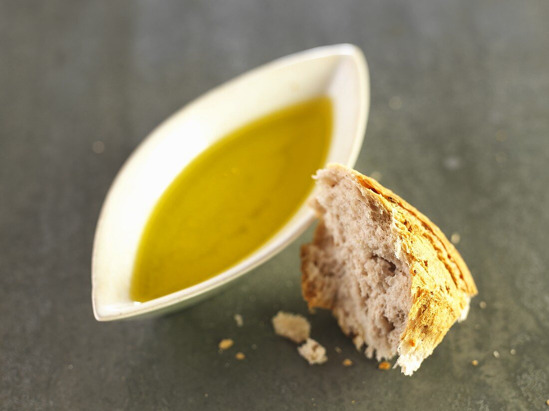 A small dish of olive oil and a piece of bread roll