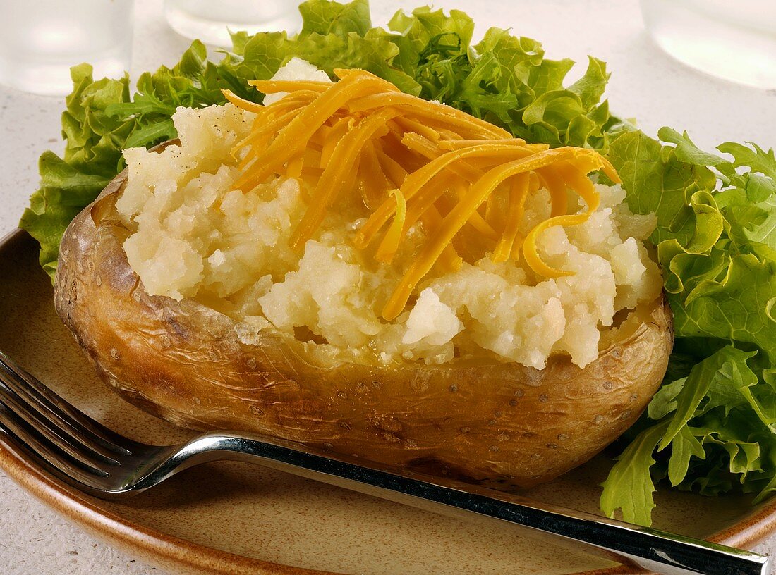 A baked potato with grated Cheddar cheese