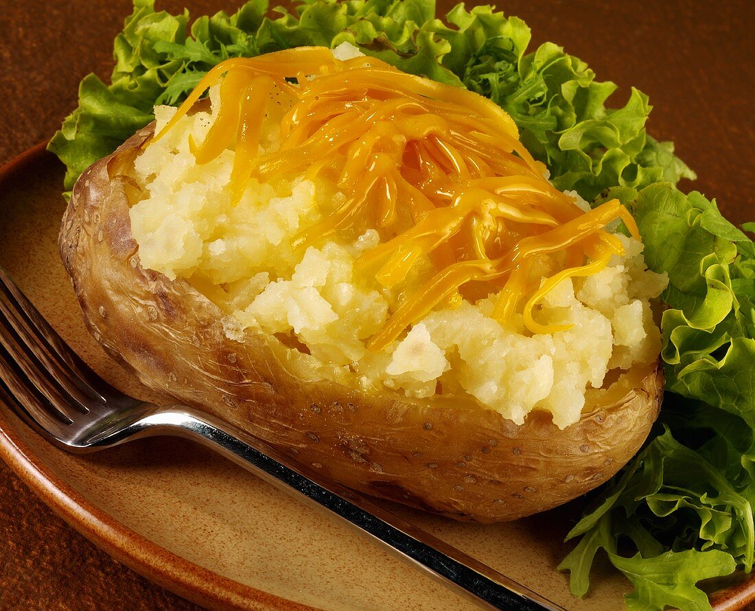 A baked potato with grated Cheddar cheese