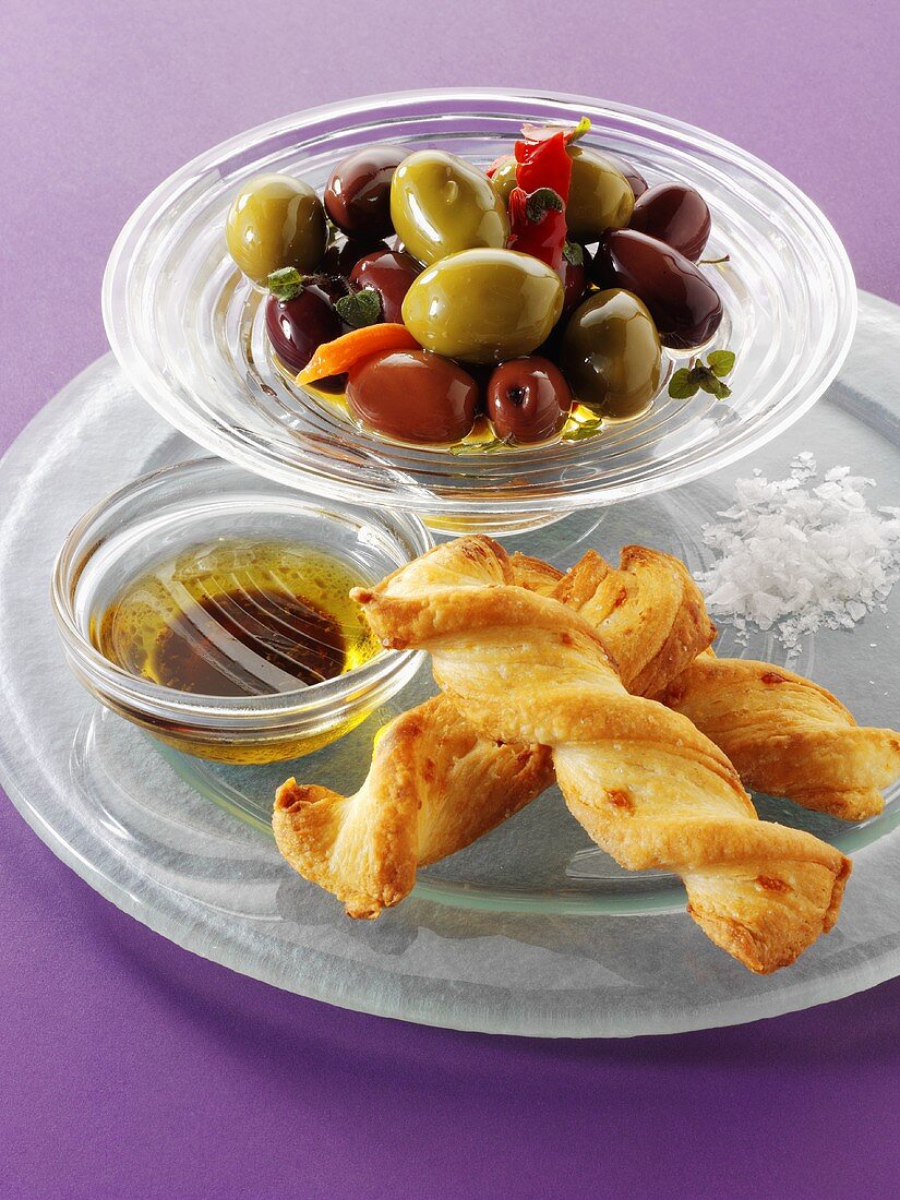 Marinated olives in a small glass dish with cheese straws