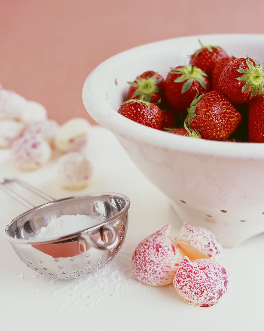 Frische Erdberen in einem Küchensieb, Meringues, Puderzucker
