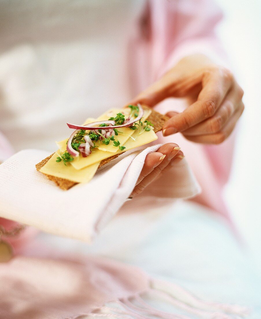 Woman holding crispbread with cheese and onion on fabric napkin