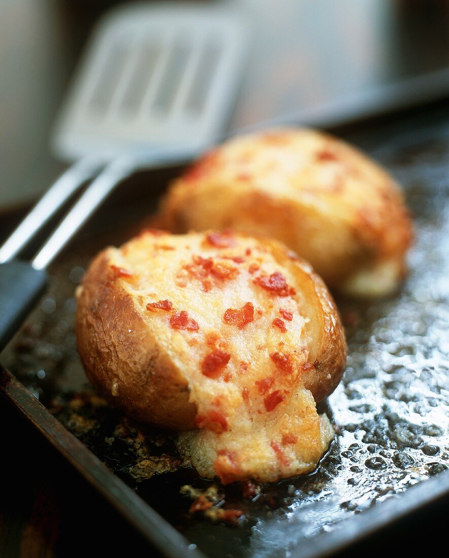 Baked potatoes with cheese and bacon filling on a baking tray