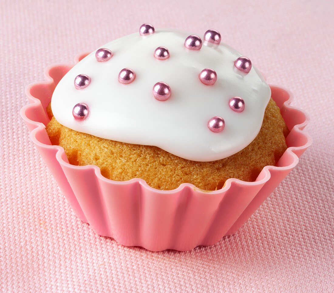 Cupcake mit weisser Glasur und rosa Zuckerperlen
