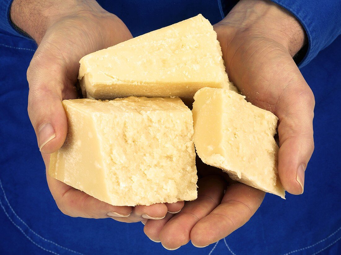 Hands holding three pieces of Parmesan