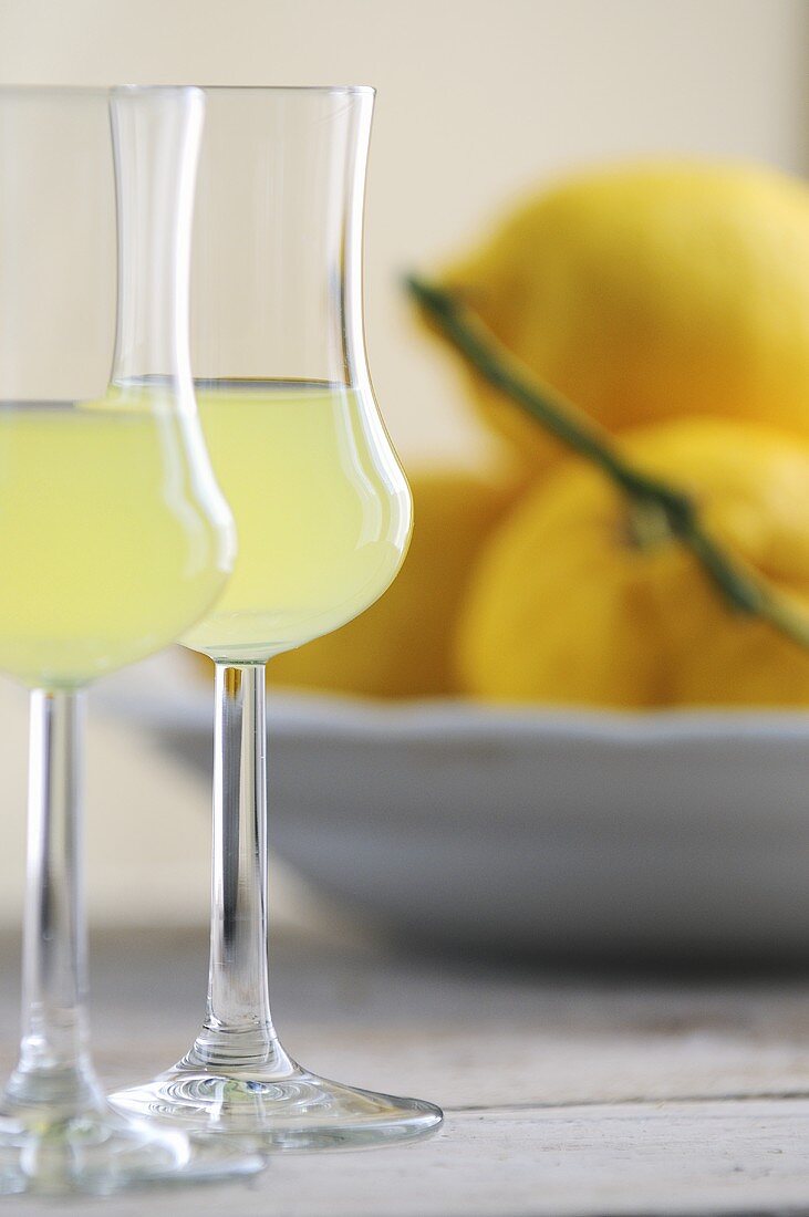 Zwei Gläser Limoncello, frische Zitronen im Hintergrund