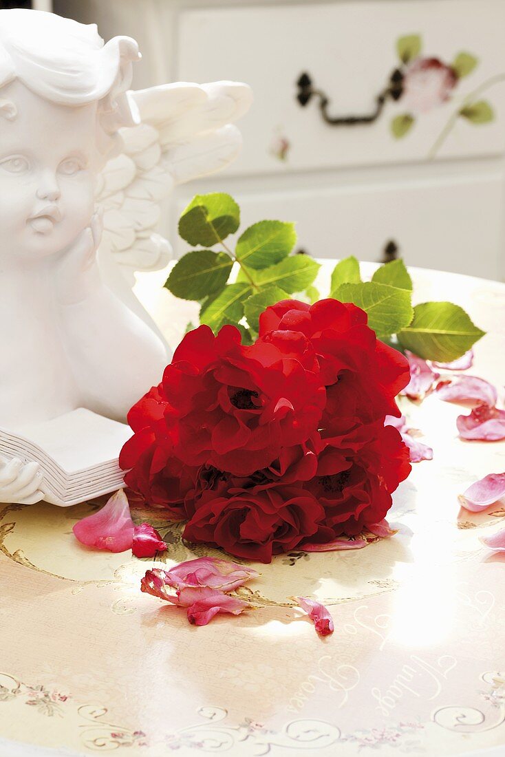 A small round bouquet of red roses beside an angel bust