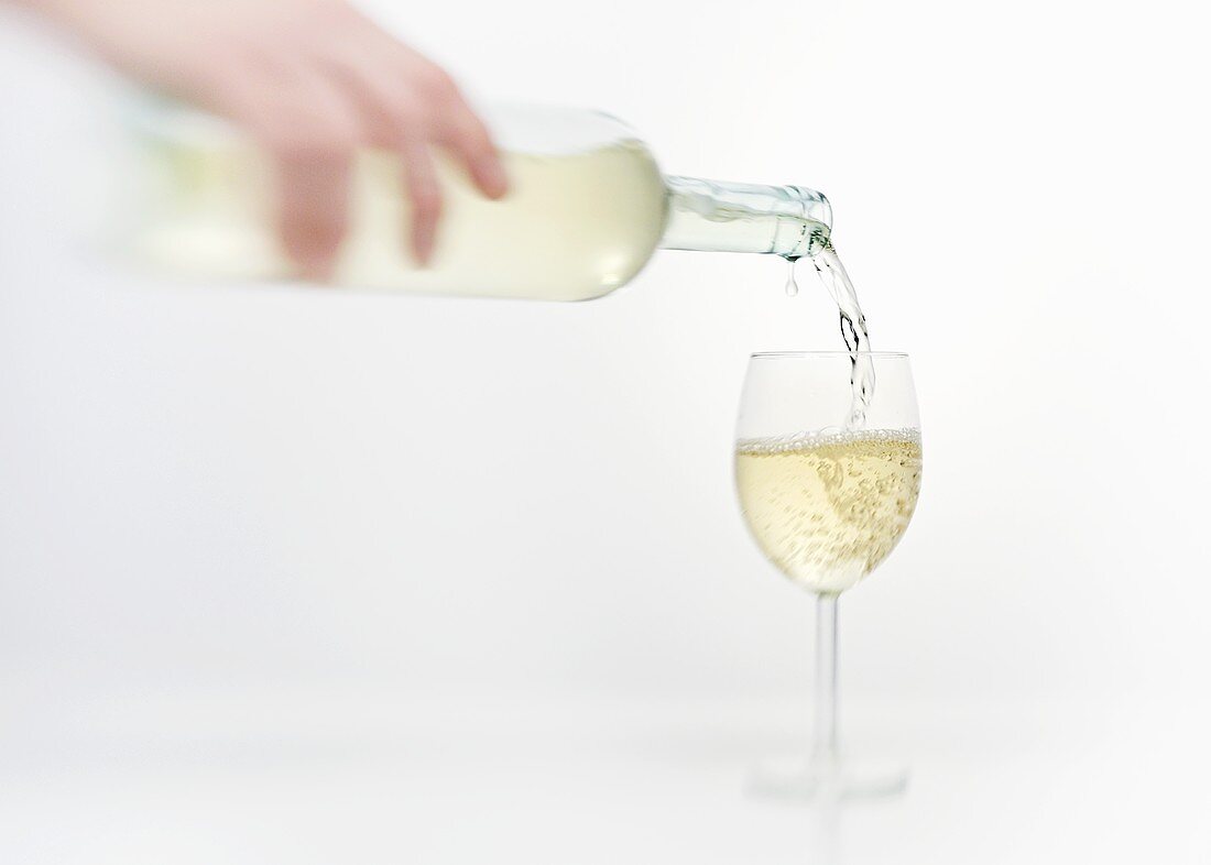 Weißwein wird in ein Weinglas eingeschenkt