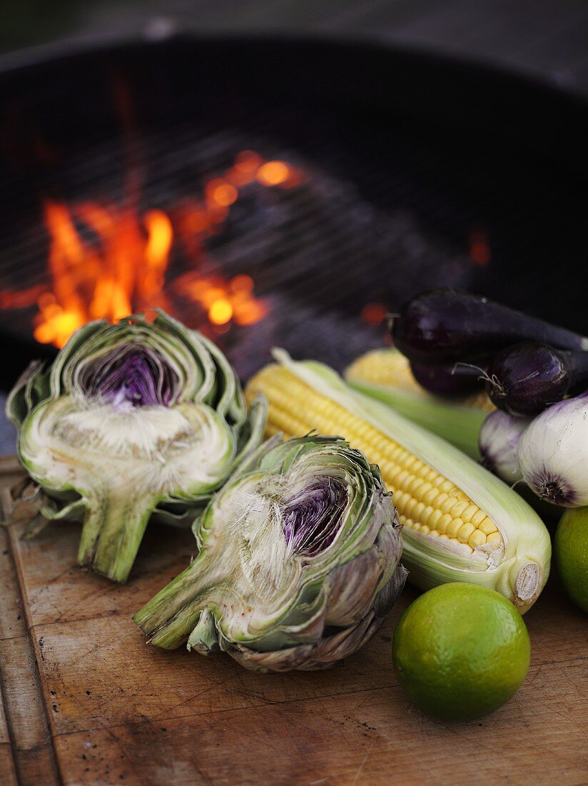 Vegetables, corn on the cob & limes beside charcoal barbecue