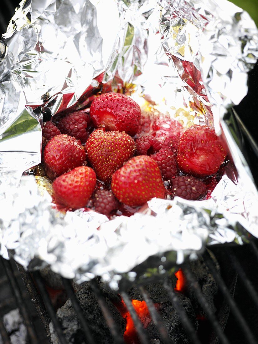 Strawberries and raspberries in aluminium foil on barbecue