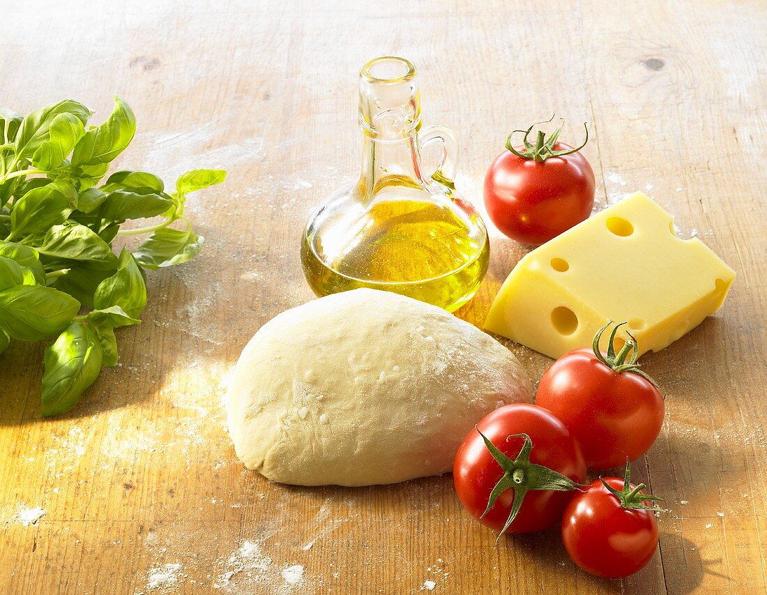 Stillleben mit Pizzateig, Tomaten, Käse, Olivenöl, Basilikum