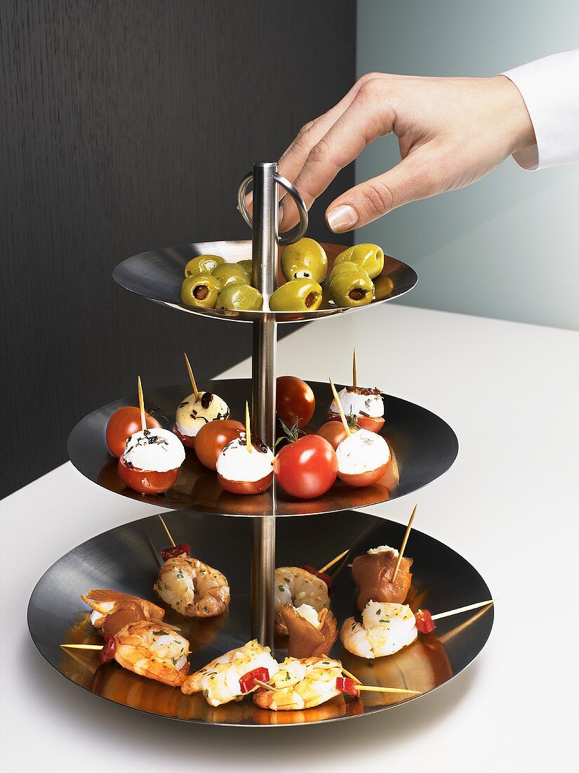 Hand reaching for olives on tiered stand with appetisers