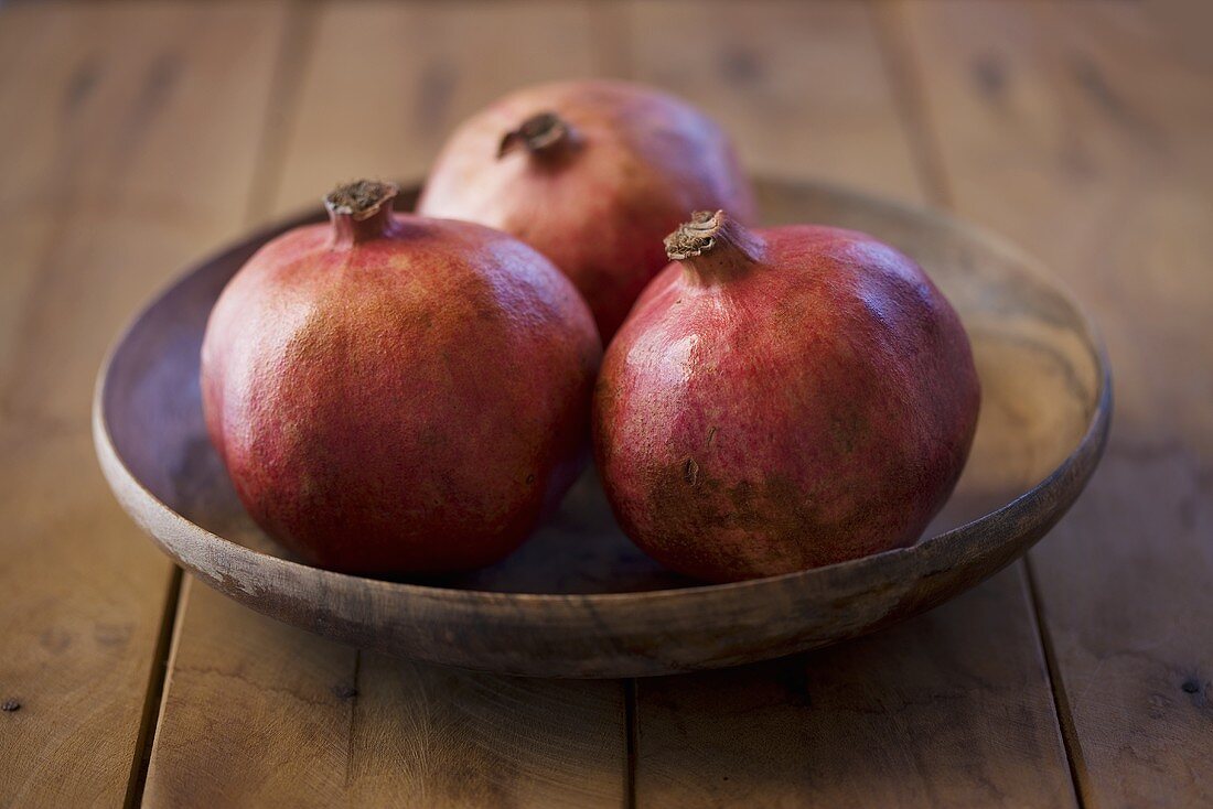 Three pomegranates in a wooden dish