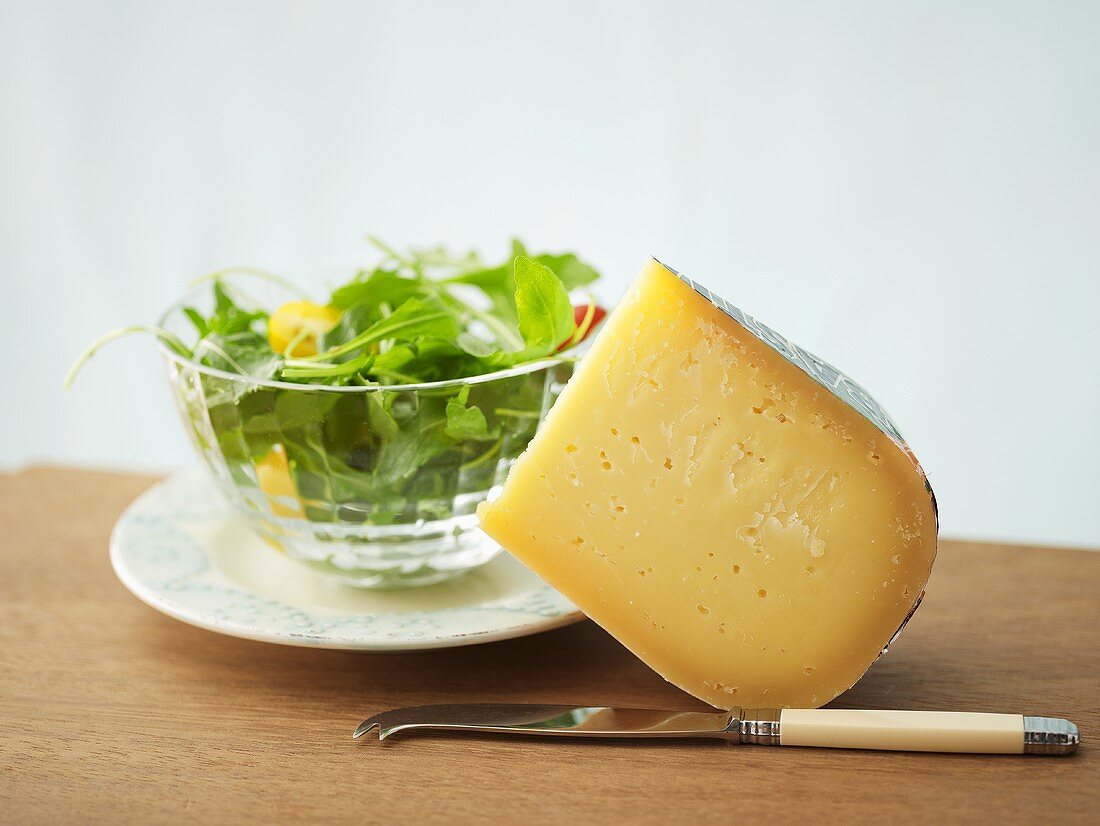 A piece of Gouda cheese with rocket salad in background