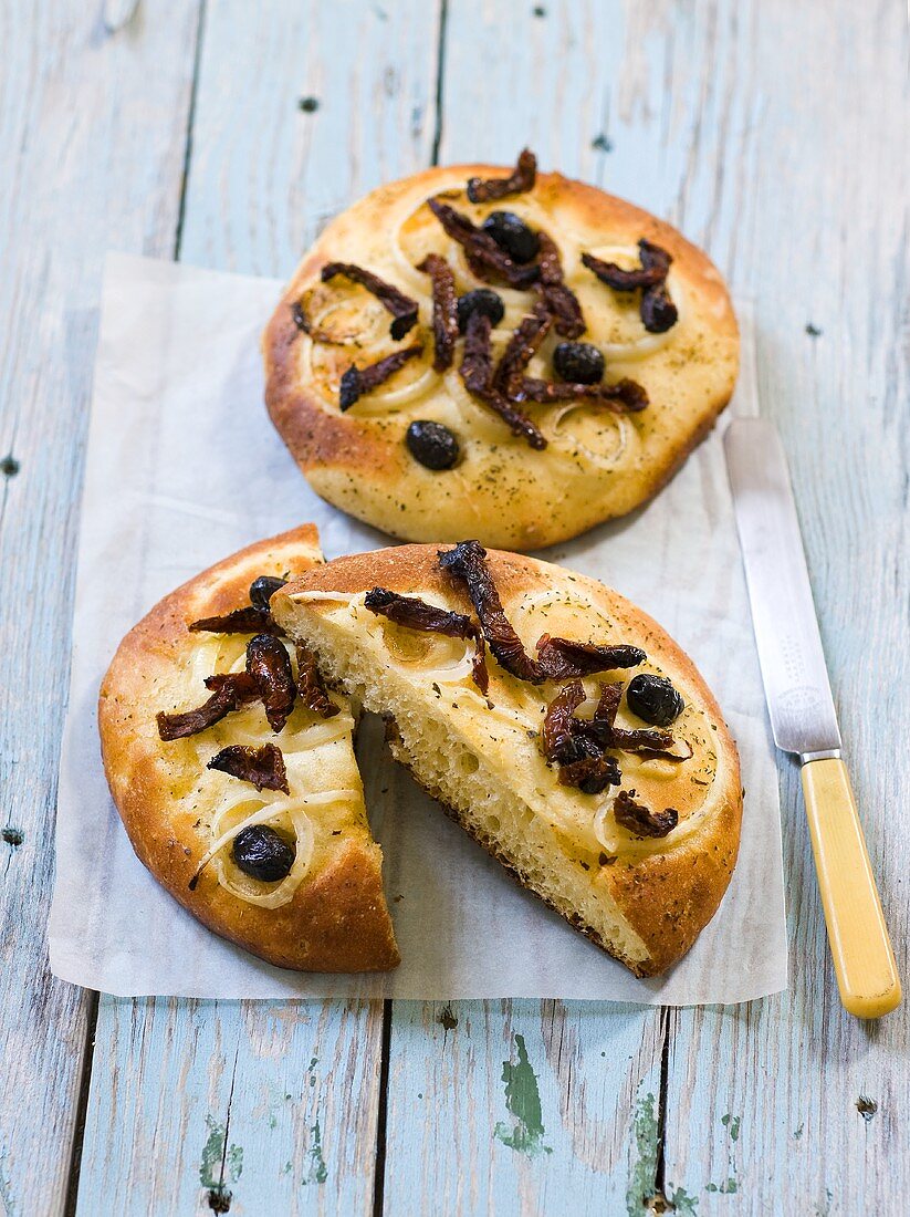 Zwei Focaccia mit Oliven, Speck und Zwiebeln