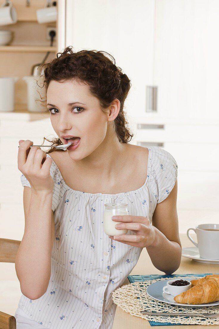 Young woman eating yoghurt for breakfast