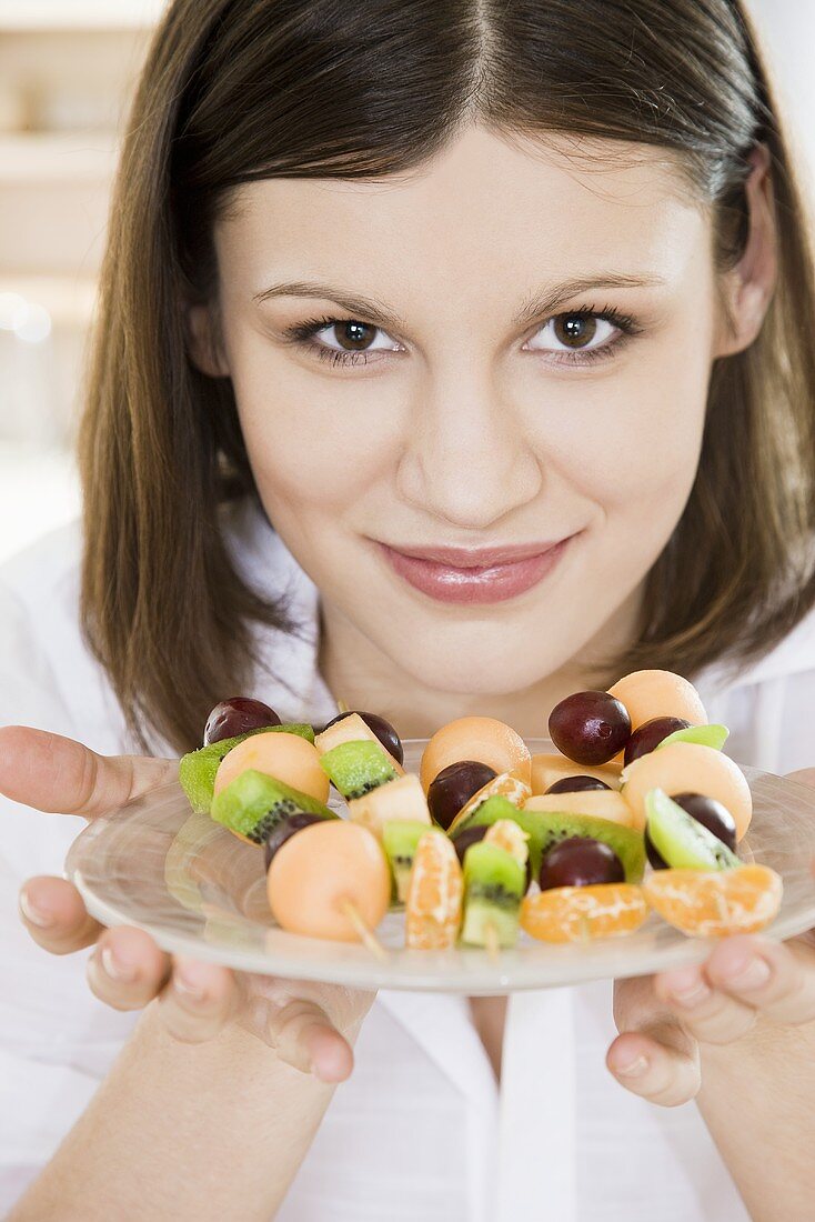 Young woman holding plate of fruit skewers