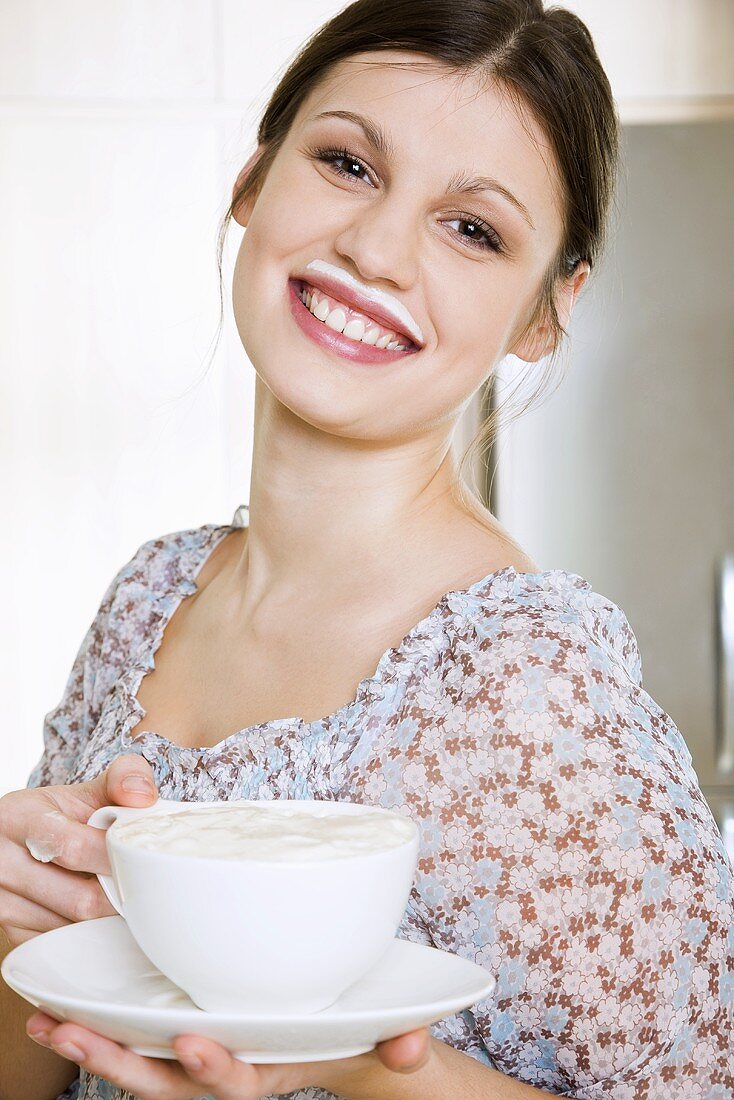 Junge Frau hält eine Tasse Kaffee mit Milchschaum
