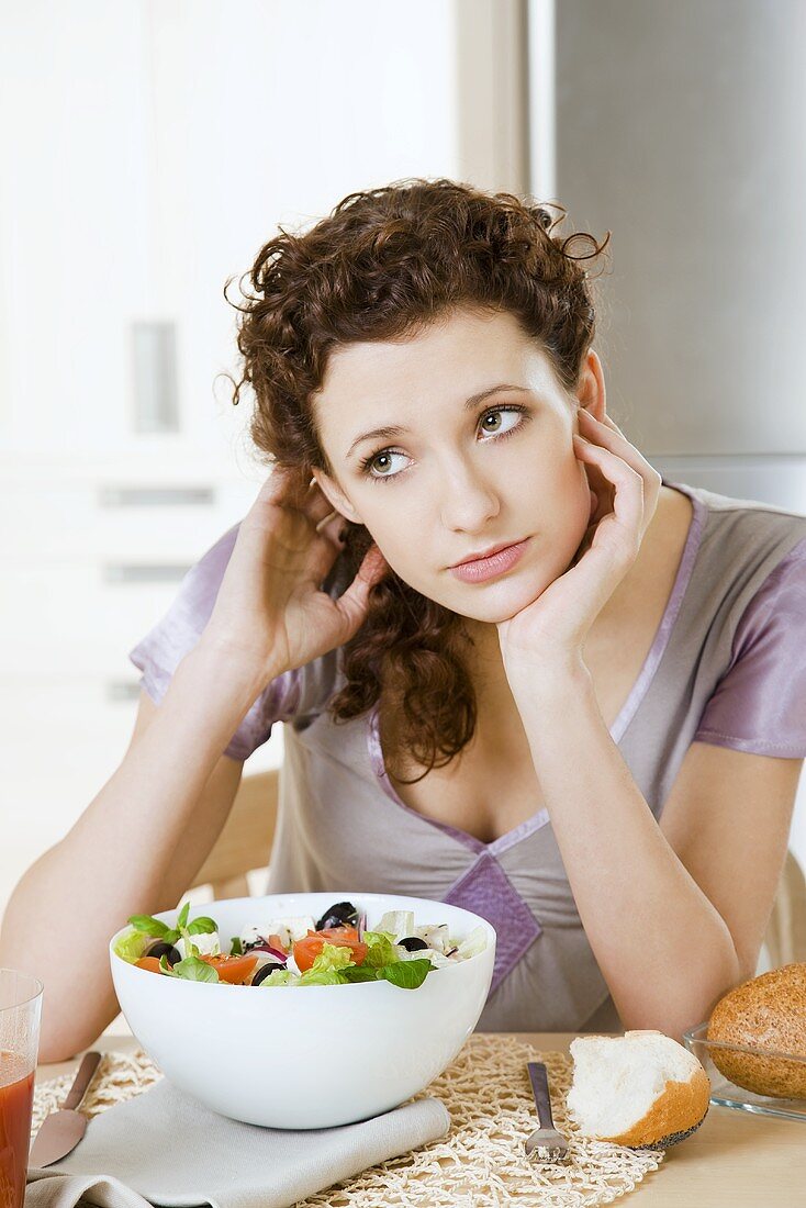 Junge Frau sitzt am Tisch mit griechischem Salat
