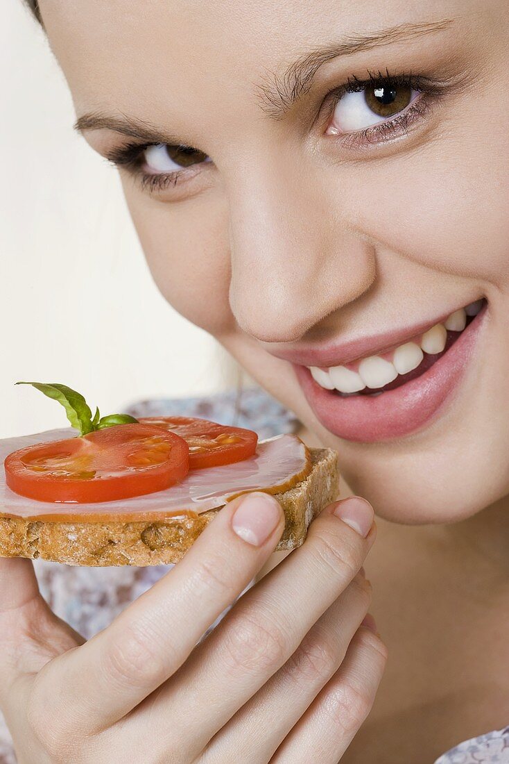 Junge Frau isst Vollkornbrot mit Schinken und Tomaten