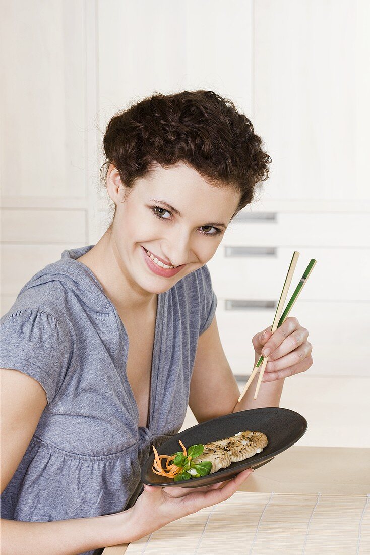 Young woman eating fried fish with chopsticks