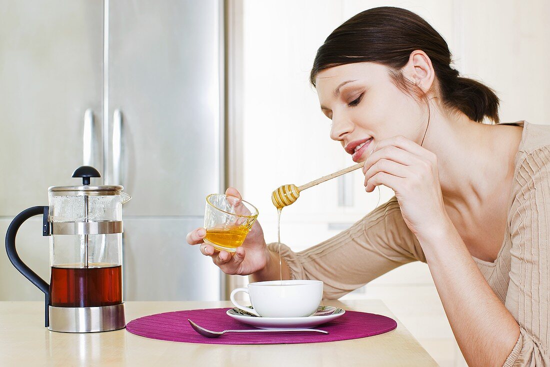 Young woman sweetening her tea with honey