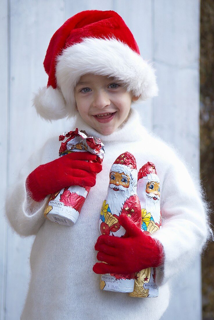 Junge mit Nikolausmütze hält Schokoladenweihnachtsmänner