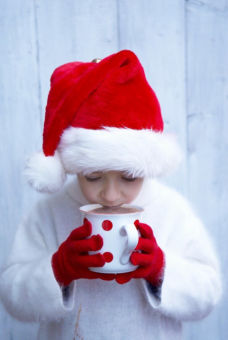 Boy in Father Christmas hat drinking mug of hot chocolate