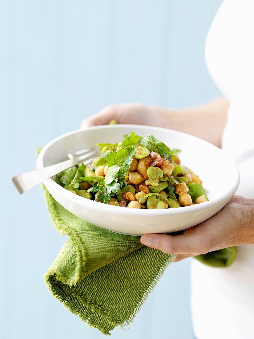 Woman holding dish of bean & chick-pea salad with coriander