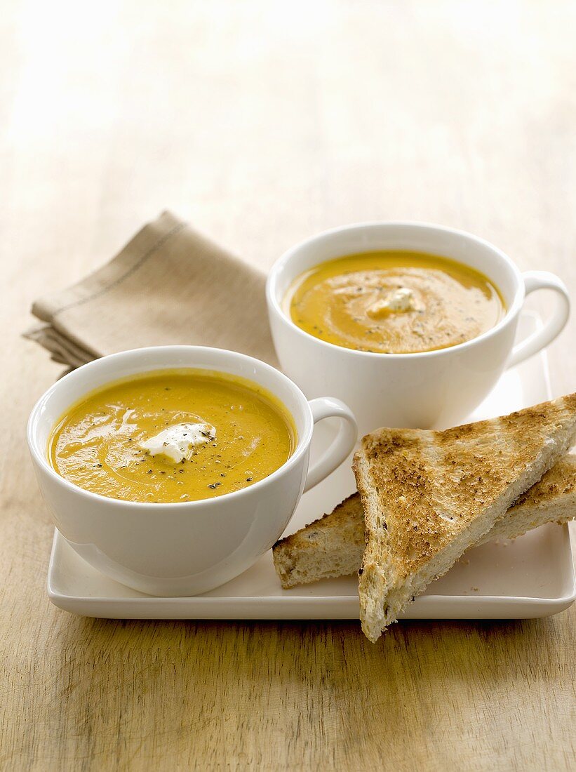 Two cups of carrot and lentil soup with toast triangles