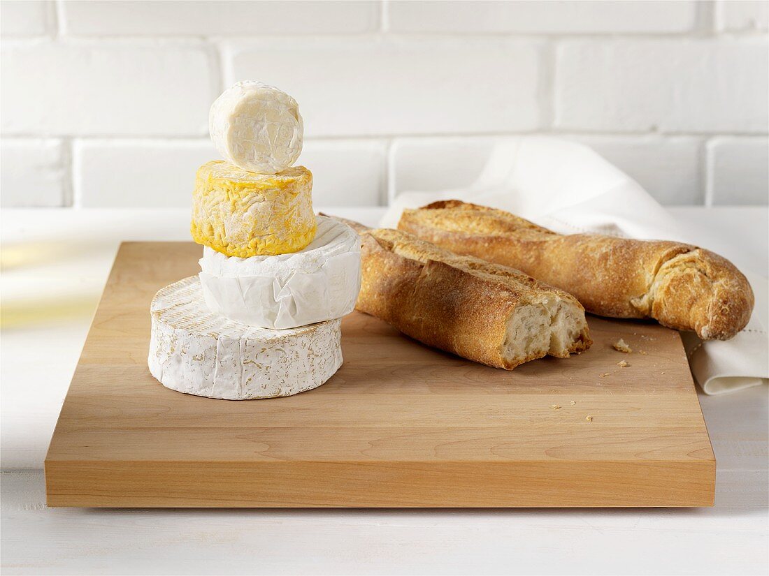 A selection of soft cheeses and baguette on chopping board