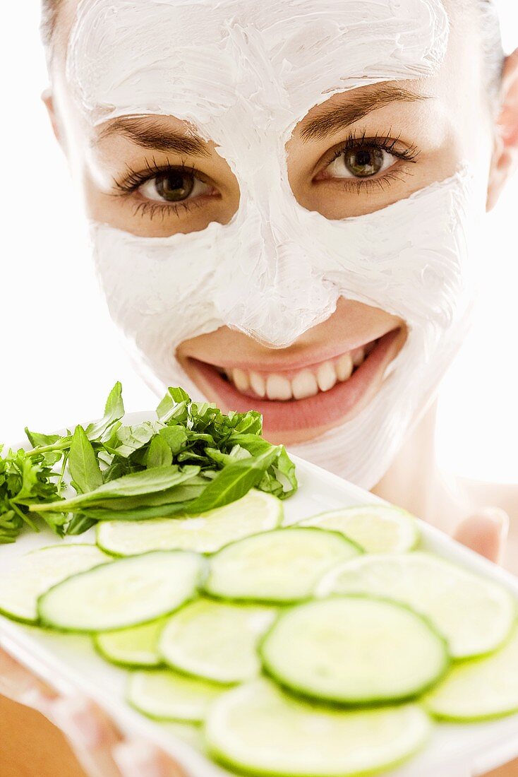 Woman with facial mask holding tray of vegetables & herbs