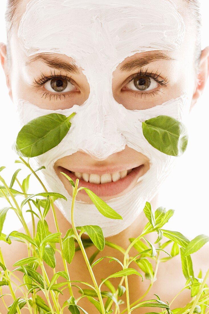 Young woman with herbal facial mask and fresh herbs