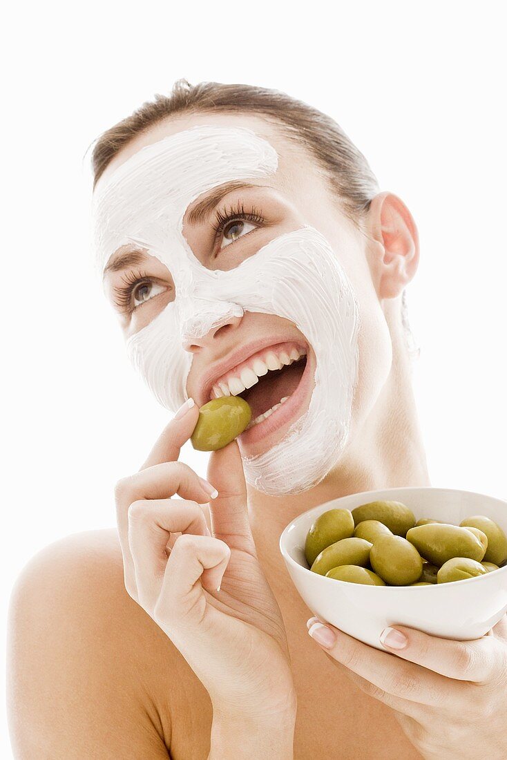 Junge Frau mit Gesichtsmaske isst grüne Oliven
