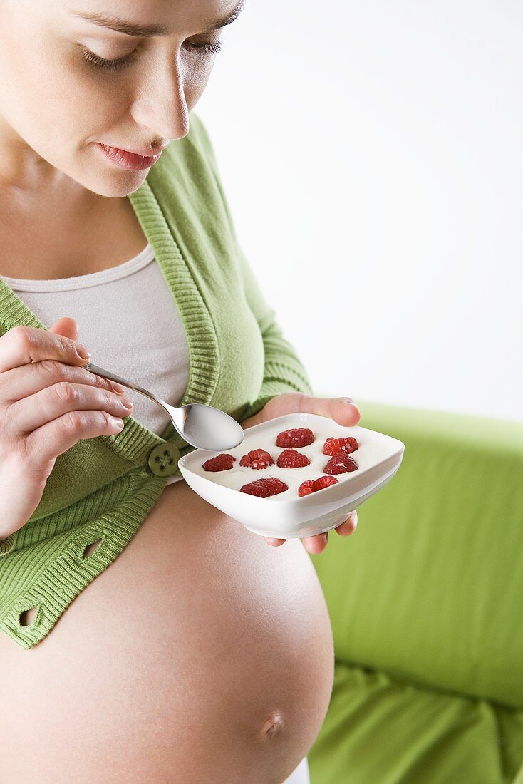 Schwangere Frau isst Joghurt mit Himbeeren