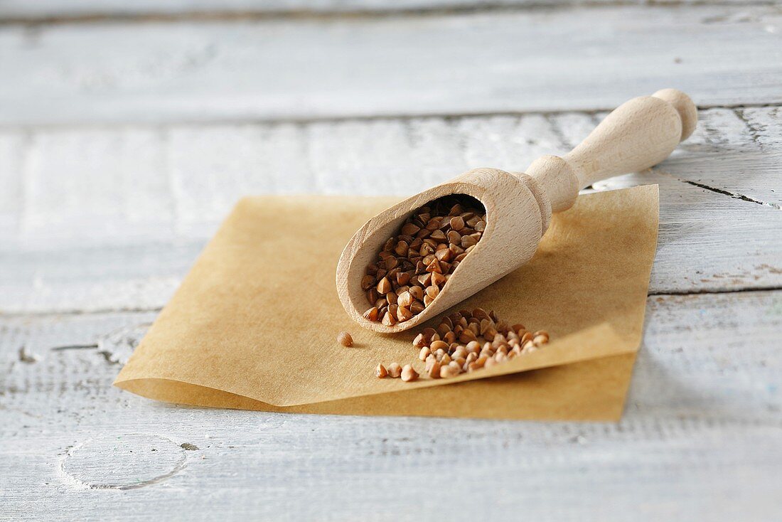 Buckwheat in and beside a wooden scoop on baking parchment