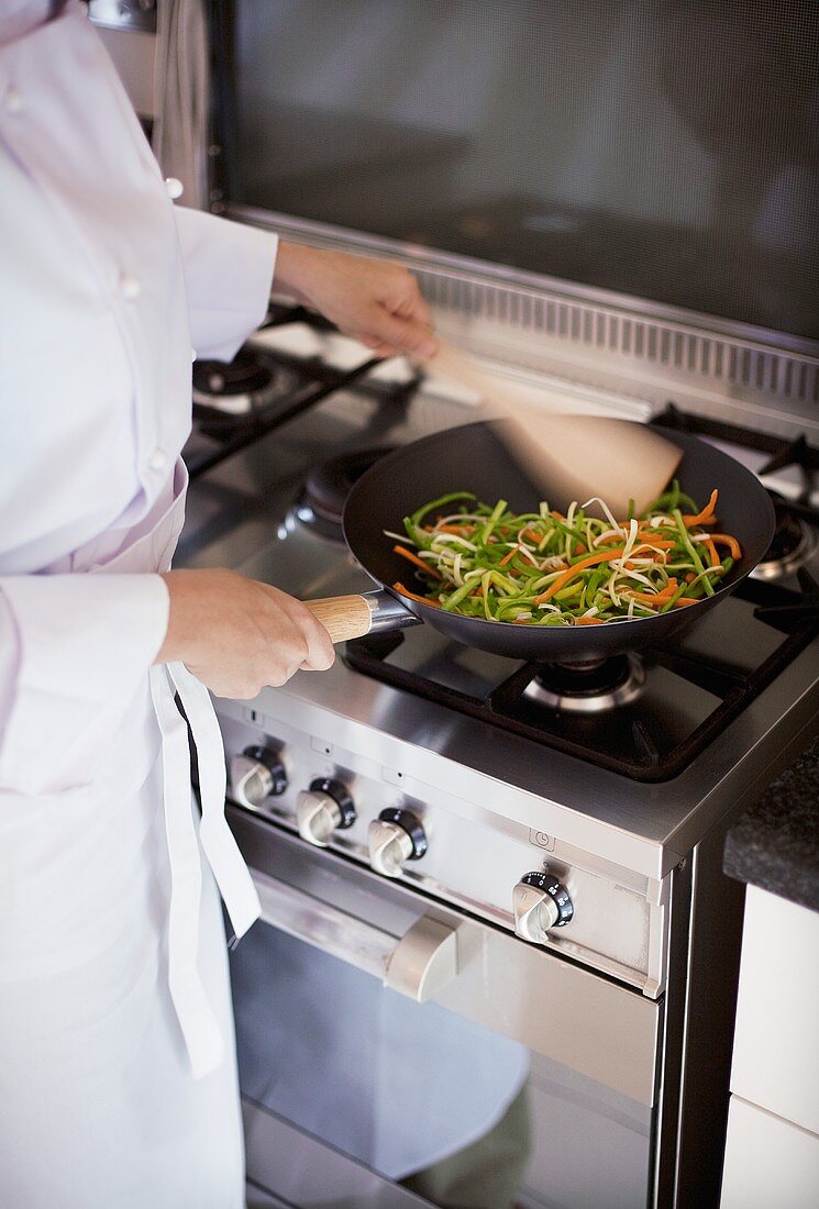 Female chef stir-frying vegetables in wok on gas cooker